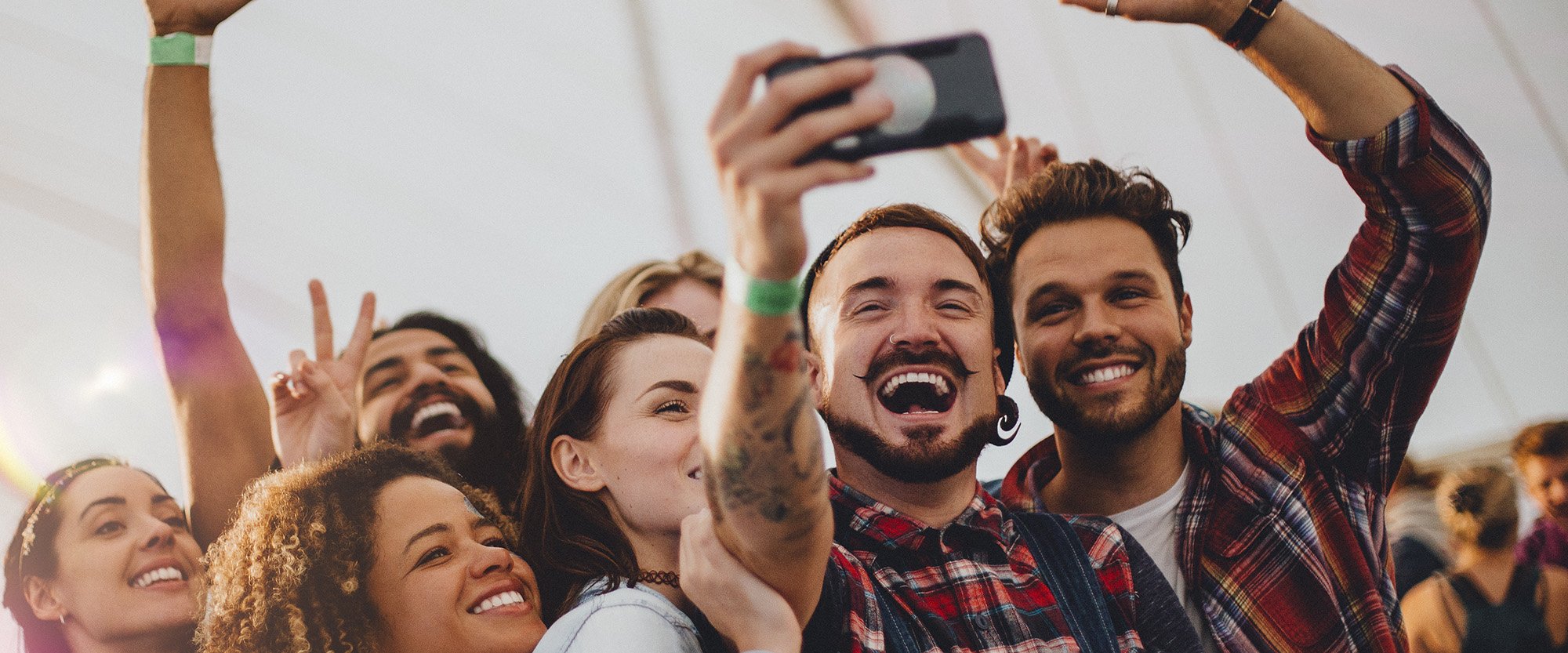 Group of young adult friends are taking a group selfie on a smartphone while they are at a festival looking for social media data