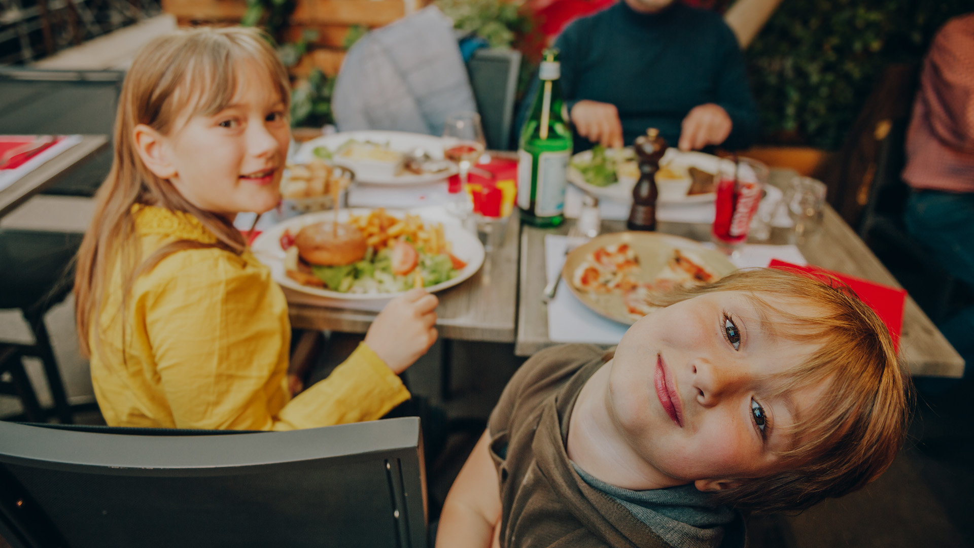 Happy family eating hamburger with french fries and pizza in outdoor restaurant